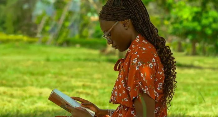 dark brown-skinned Black woman reading outside on a blanket